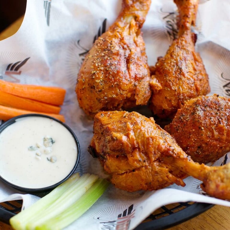 Basket of seasoned chicken wings with carrot and celery sticks alongside creamy dipping sauce on a restaurant table.