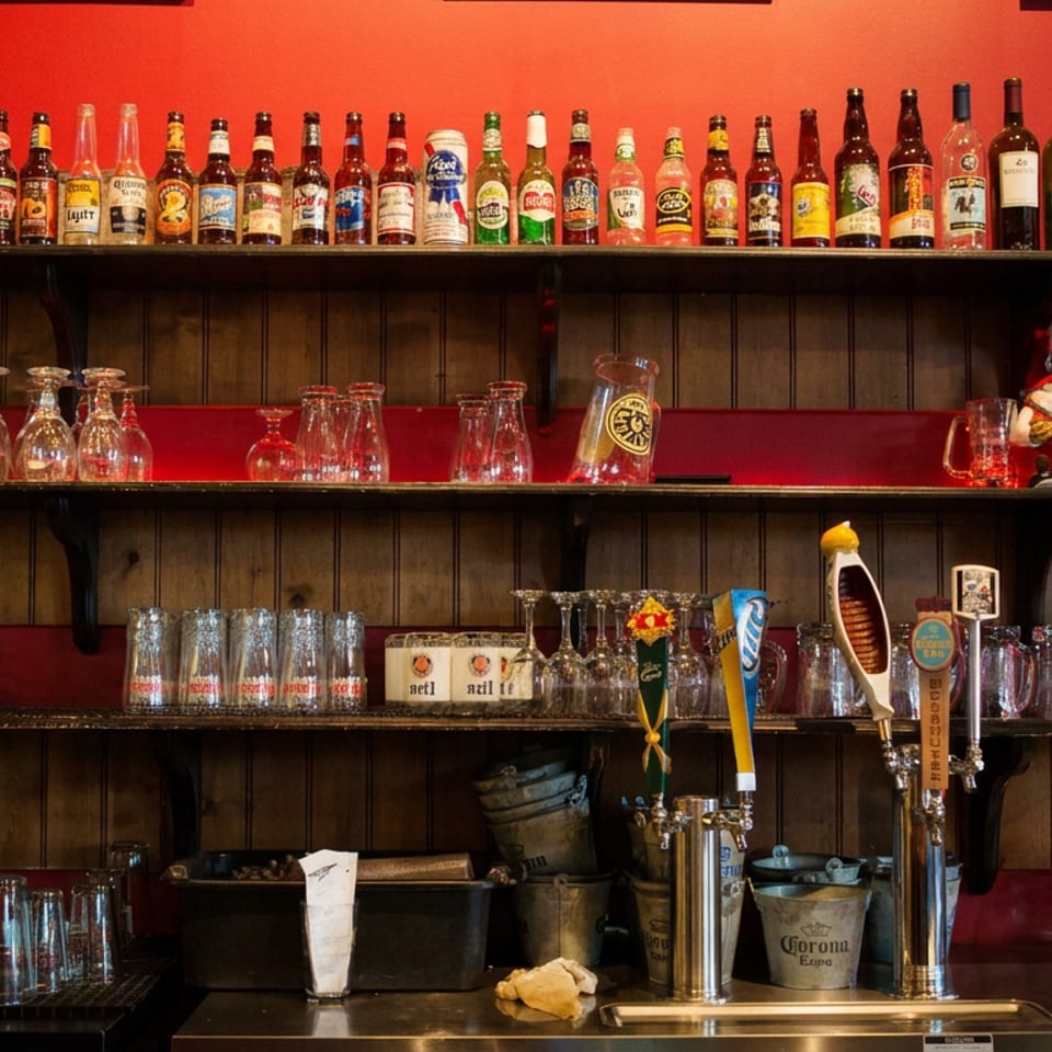 Colorful restaurant bar with beer bottles, glassware, beer taps, and memorabilia arranged against red and wood-paneled walls.
