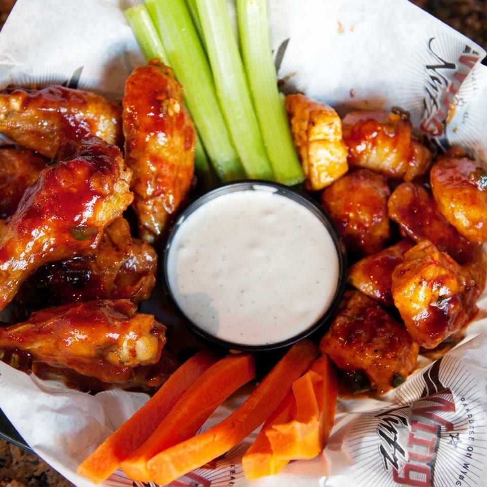 Glazed chicken wings served with celery, carrot sticks, and ranch dipping sauce in a lined basket.